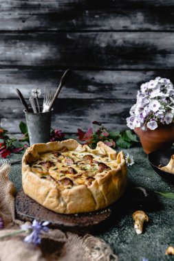 delicious pie with mushrooms and potted flowers on wooden table clipart