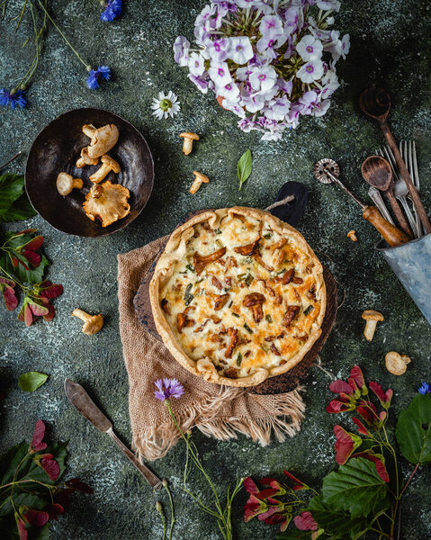 top view of appetizing quiche with mushrooms and potted flowers on wooden table