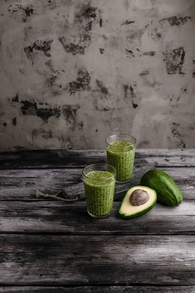 Organic smoothie in glasses by cut avocado on wooden background — Stock Photo