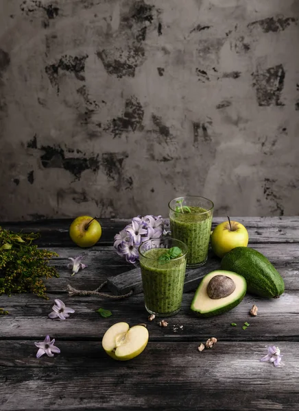 Grüne Frucht-Smoothie in Gläsern auf Holzgrund mit Blumen — Stockfoto