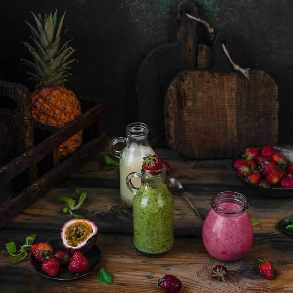 Batidos de frutas ecológicas sobre fondo de madera con piña y bayas - foto de stock