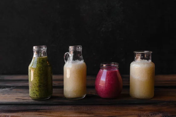 Набор бутылок со свежими здоровыми коктейлями на деревенском столе — стоковое фото