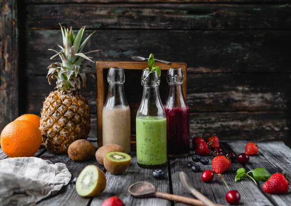 Frullati di frutta biologica in bottiglie di vetro su fondo di legno con frutta assortita — Foto stock