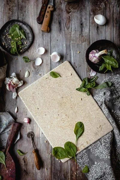 Top view of wooden board, herbs, garlic and utensils on wooden table — Stock Photo