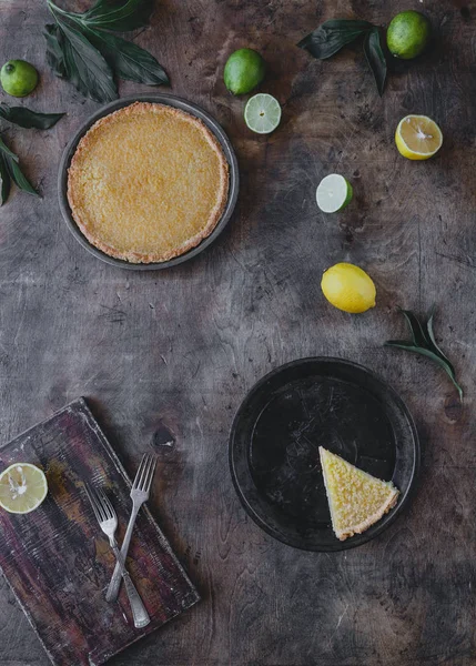 Повышенный вид на вкусный лимонный пирог и лаймы с лимонами на деревянном столе — стоковое фото