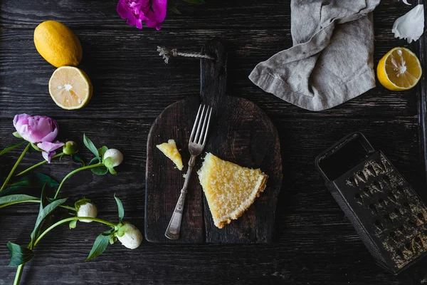 Blick von oben auf ein Stück leckeren Zitronenkuchen und Blumen auf dem Holztisch — Stockfoto