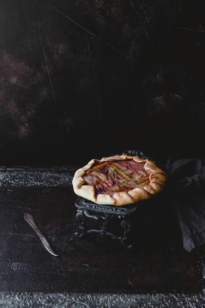 Tasty rhubarb pie on dark cake stand on table — Stock Photo