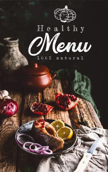 Baked salmon steak with lemon and onion on plate with pomegranate on wooden table, healthy menu lettering — Stock Photo