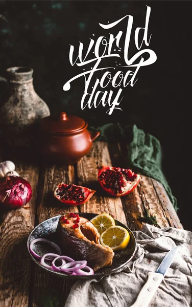Gebackenes Lachssteak mit Zitrone und Zwiebel auf Teller mit Granatapfel auf Holztisch, Schriftzug Welternährungstag — Stockfoto