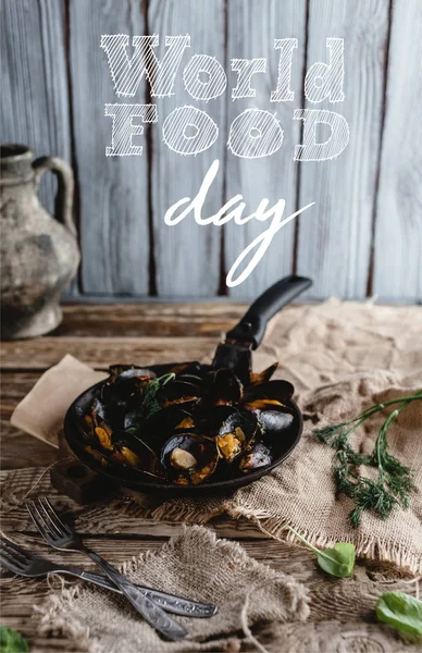Gourmet gebratene Miesmuscheln mit Schalen auf Pfanne und Gabeln auf Tisch, Schriftzug zum Welternährungstag — Stockfoto