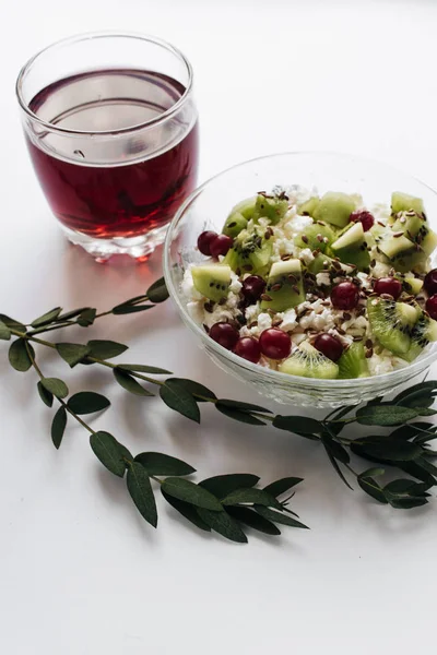 delicious cottage cheese with kiwi pieces and cranberries in bowl and glass of juice on white background, closeup, healthy breakfast