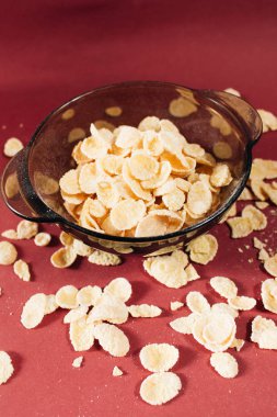 Kırmızı arka planda kasede mısır gevreği ve sağlıklı bir kahvaltı.