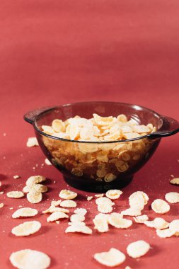 Kırmızı arka planda kasede mısır gevreği ve sağlıklı bir kahvaltı.