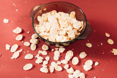 Kırmızı arka planda kasede mısır gevreği ve sağlıklı bir kahvaltı.