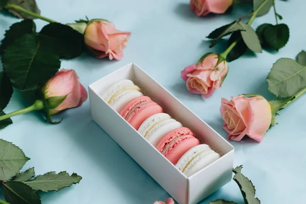 composition of delicious macaroons and pink roses on blue table