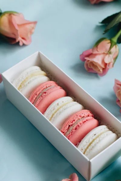 composition of delicious macaroons and pink roses on blue table