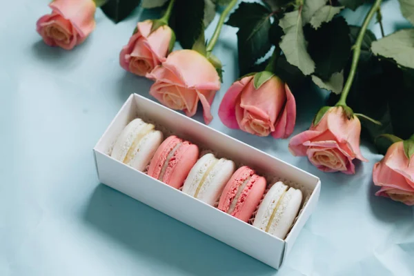 composition of delicious macaroons and pink roses on blue table