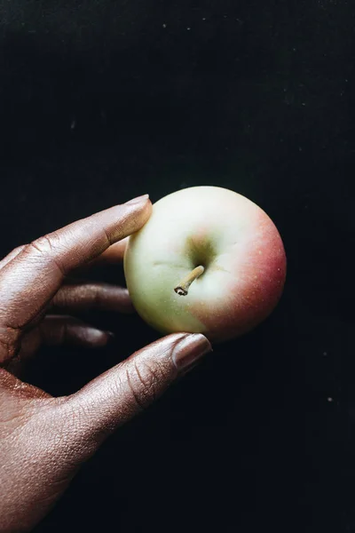female hand holding apple on black background