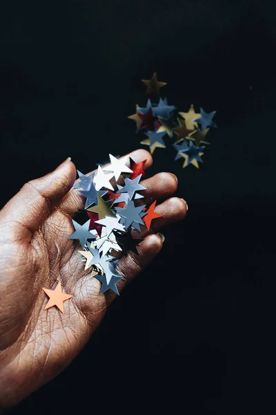female hand holding stars confetti, black background