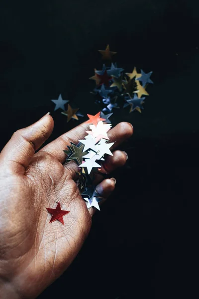 female hand holding stars confetti, black background