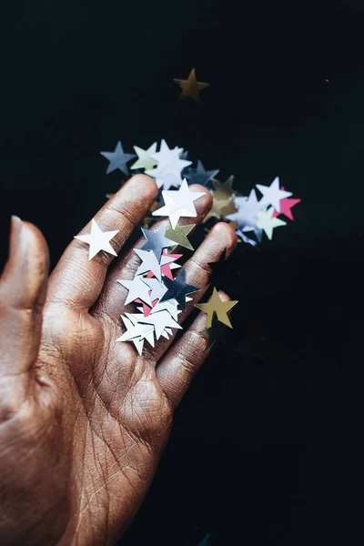 female hand holding stars confetti, black background