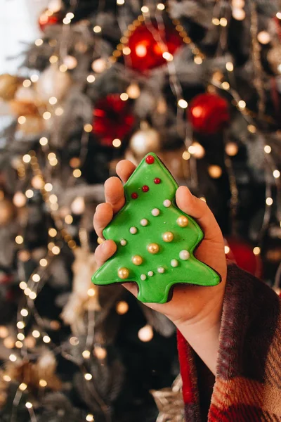 female hand holding glazed cookie shaped as Christmas tree