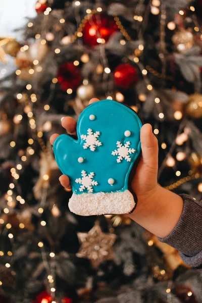 female hand holding glazed cookie shaped as blue mitten