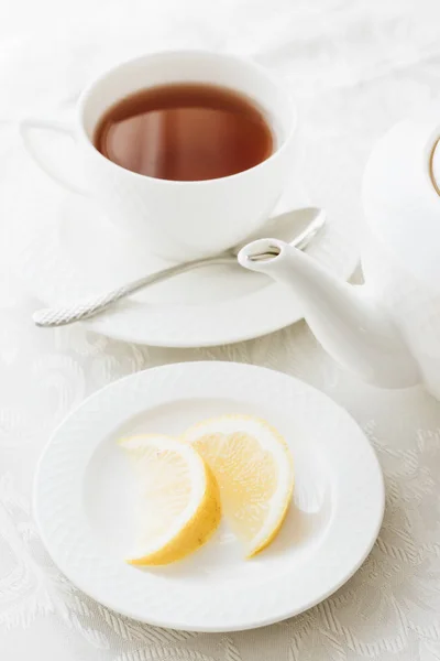 white tea equipage, cup of tea, white teapot, sliced lemon on saucer