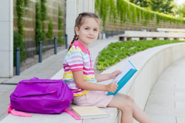 Okulun ilk günü. Elinde kitap olan ilkokul öğrencisi. . Binanın yanında sırt çantası olan bir kız. Derslerin başlangıcı. Sonbaharın ilk günü. okula geri kavram.