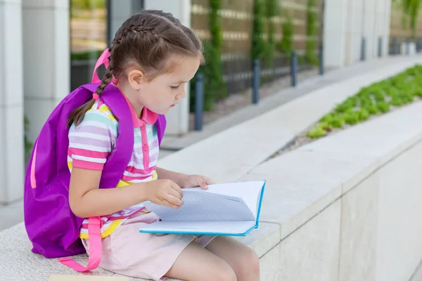 Okulun ilk günü. Elinde kitap olan ilkokul öğrencisi. . Binanın yanında sırt çantası olan bir kız. Derslerin başlangıcı. Sonbaharın ilk günü. okula geri kavram.