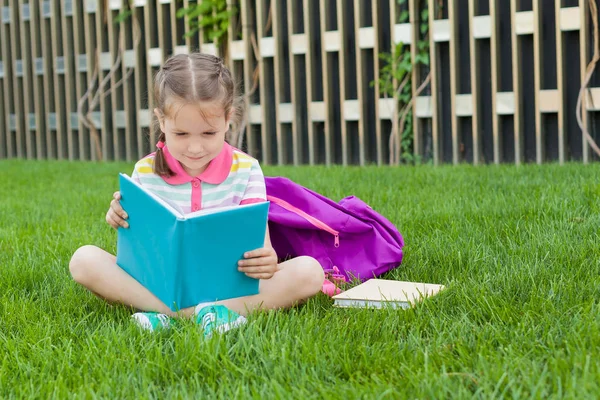 First day of school. child girl schoolgirl elementary school student sitting on the grass near the school and read book. Concept back to school. outdoor activities