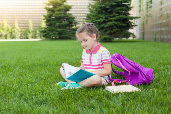 First day of school. child girl schoolgirl elementary school student sitting on the grass near the school and draws in a notebook. Concept back to school. outdoor activities