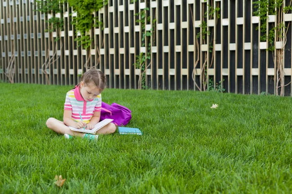 First day of school. child girl schoolgirl elementary school student sitting on the grass near the school and draws in a notebook. Concept back to school. outdoor activities