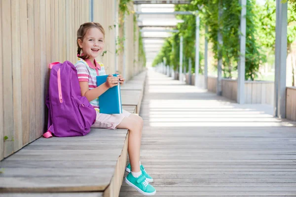 Okulun ilk günü. Elinde kitap olan ilkokul öğrencisi. . Binanın yanında sırt çantası olan bir kız. Derslerin başlangıcı. Sonbaharın ilk günü. okula geri kavram