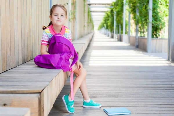 Okulun ilk günü. Elinde kitap olan ilkokul öğrencisi. . Binanın yanında sırt çantası olan bir kız. Derslerin başlangıcı. Sonbaharın ilk günü. okula geri kavram