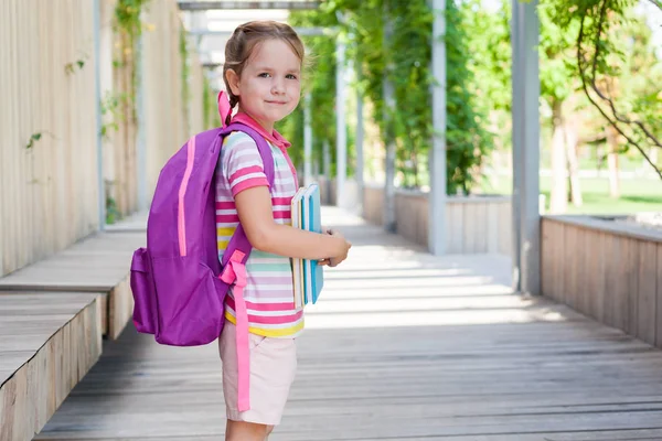 First day of school. Pupil of primary school with book in hand. . Girl with a backpack near the building  outdoor. Beginning of classes. The first day of autumn. concept back to school.