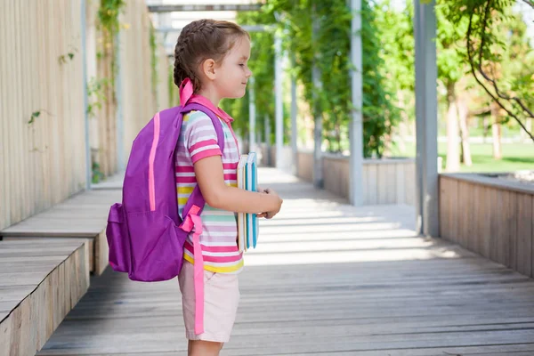 First day of school. Pupil of primary school with book in hand. . Girl with a backpack near the building  outdoor. Beginning of classes. The first day of autumn. concept back to school.