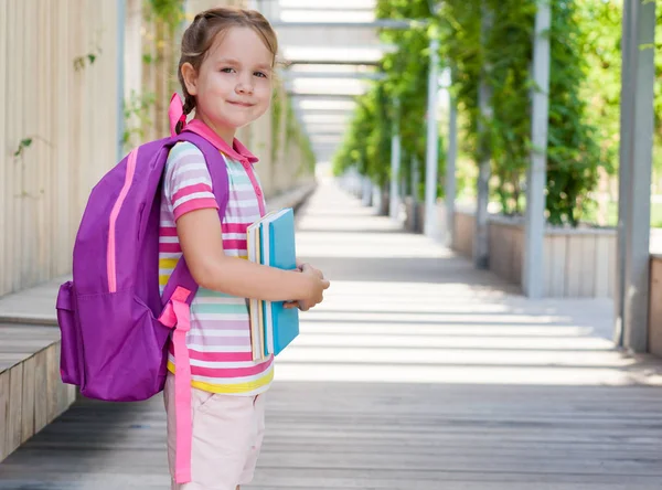 First day of school. Pupil of primary school with book in hand. . Girl with a backpack near the building  outdoor. Beginning of classes. The first day of autumn. concept back to school