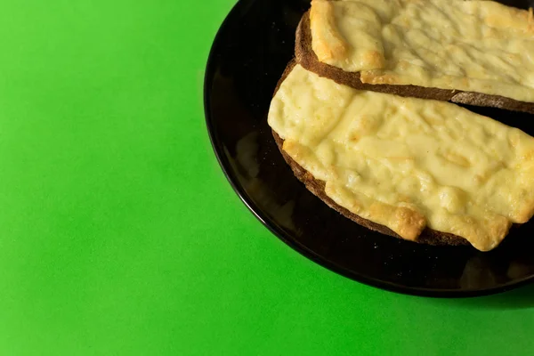 Two slices of grilled cheese on toast on black plate and bright green background- snack; melted cheese; minimal