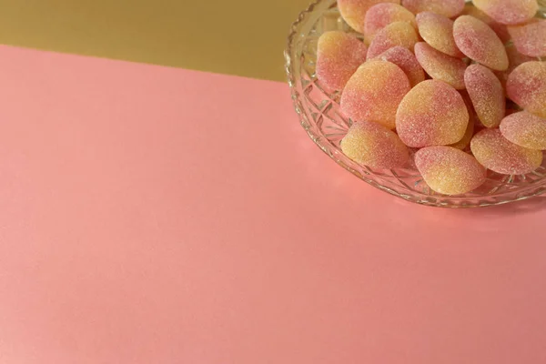 Bowl of sugared jelly sweets in crystal cut glass dish - on minimal pink and gold background - corner design element, copy space