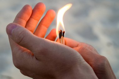 Maçlar ellerde yanma. Alev yukarı ve sol işaret maçlar. Yetişkin adam, kum arka plan.