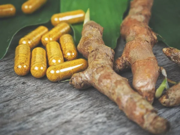 Turmeric capsule with leaves on wood background