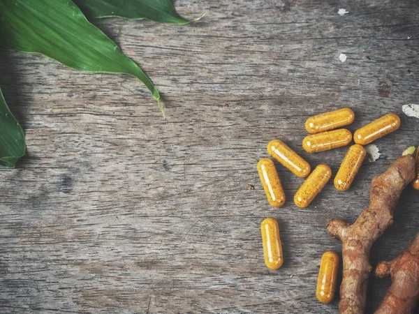 Turmeric capsule with leaves on wood background