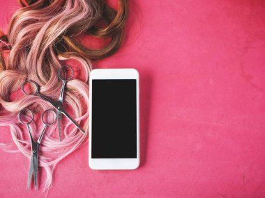 Akıllı telefon ve saç kesme makası ile pembe bir arka plan üzerinde peruk