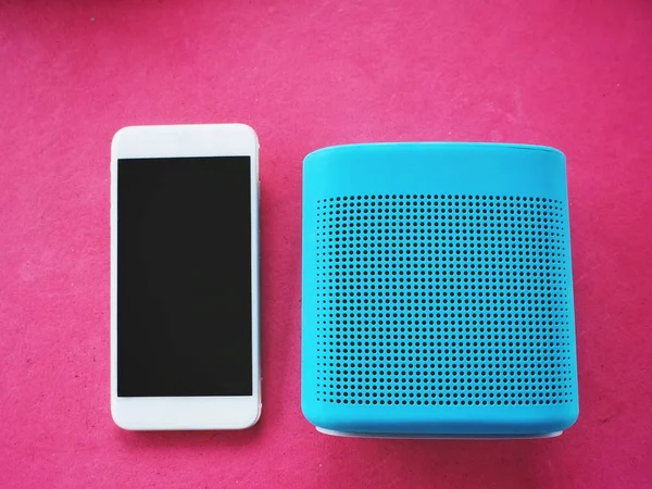 Blue bluetooth speaker and smart phone on pink background
