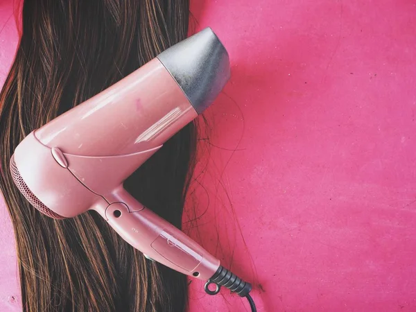 Suszarka do włosów i włosy perukę na różowym tle — Zdjęcie stockowe
