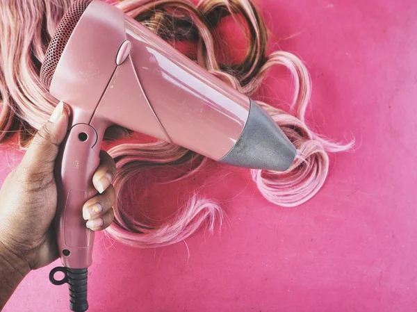 Saç kurutma makinesi ve pembe bir arka plan üzerinde peruk saç — Stok fotoğraf