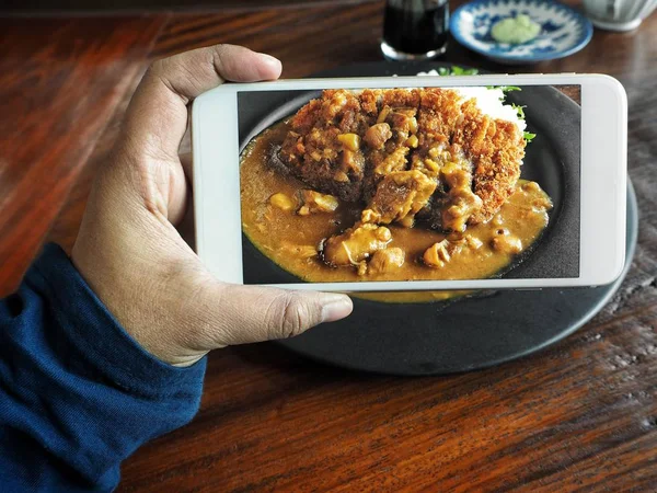 Taking a photo of curry rice and fried pork with smart phone on hand