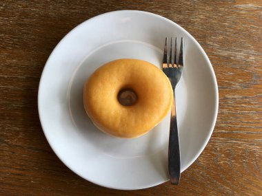 Beyaz yuvarlak seramik tabakta çelik çatallı taze, yuvarlak bir donut. Doğal ahşap arka planda yemeye ve keyfini çıkarmaya hazır.