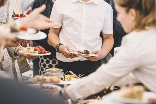 Display of sweet desserts at a celebration. People are served desserts on the plates.